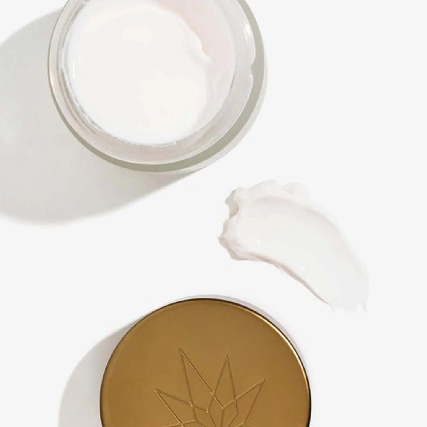 En åben pakke med CBD Natcreme + E Vitamin ligger ved siden af låget og en klat creme.
