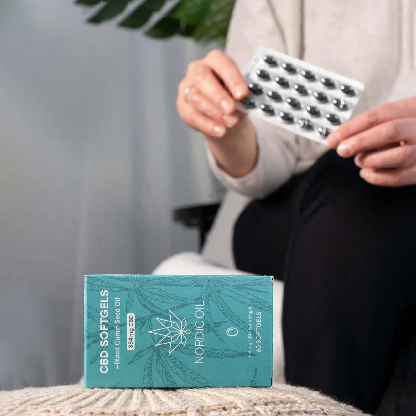 Pakke liggende på en sofa og en kunde med CBD-kapsler i baggrunden