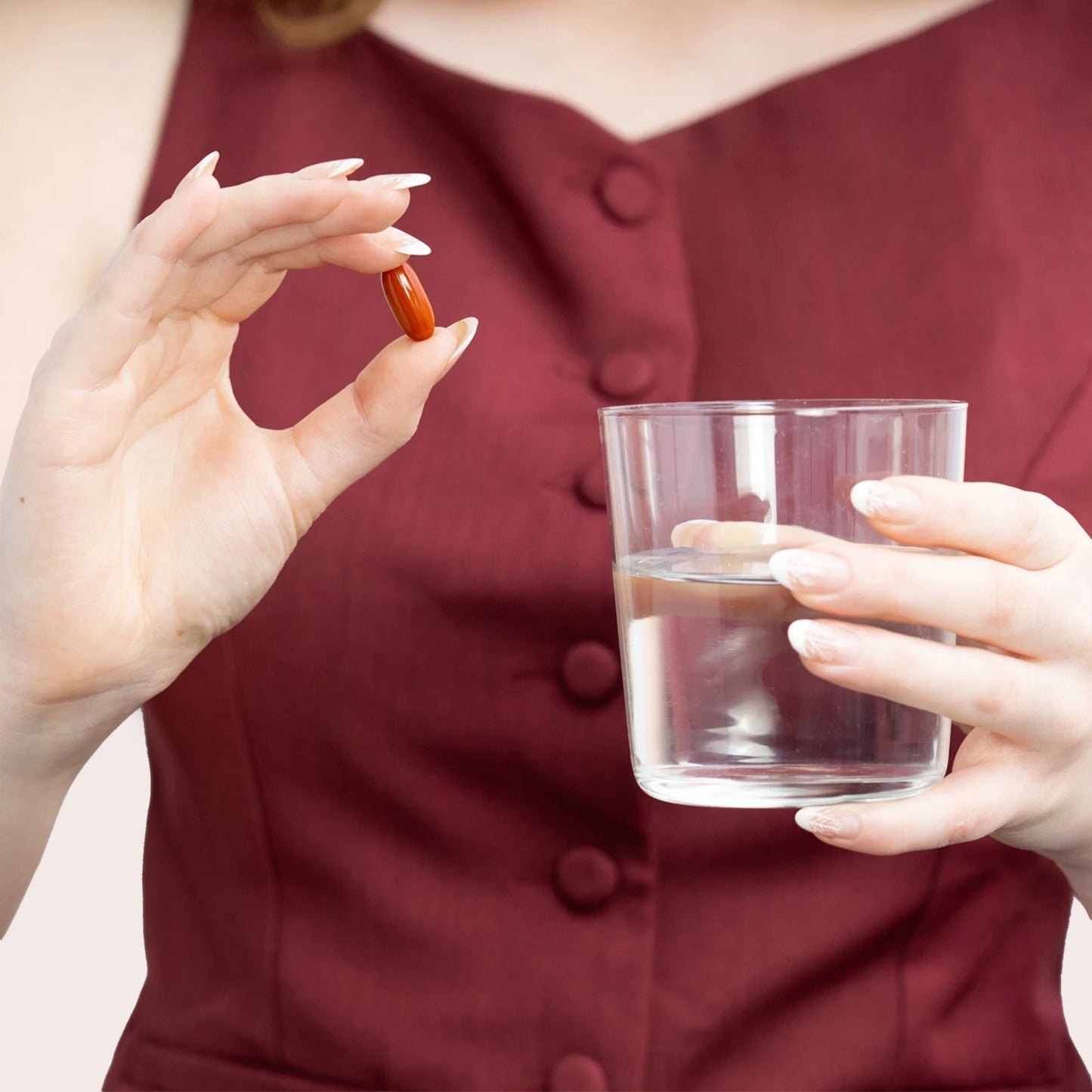 Person holder en brun kapsel mellem fingrene og et glas vand
