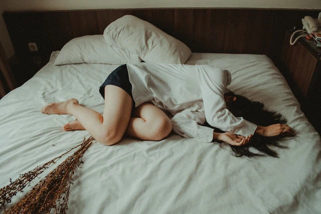 En kvinde ligger i sengen med smerter