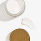 En åben pakke med CBD Natcreme + E Vitamin ligger ved siden af ​​låget og en klat creme.