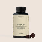 Flaske med Nordic Oil Essentials Shilajit gummies og to mørkebrune gummies ved siden af på beige baggrund