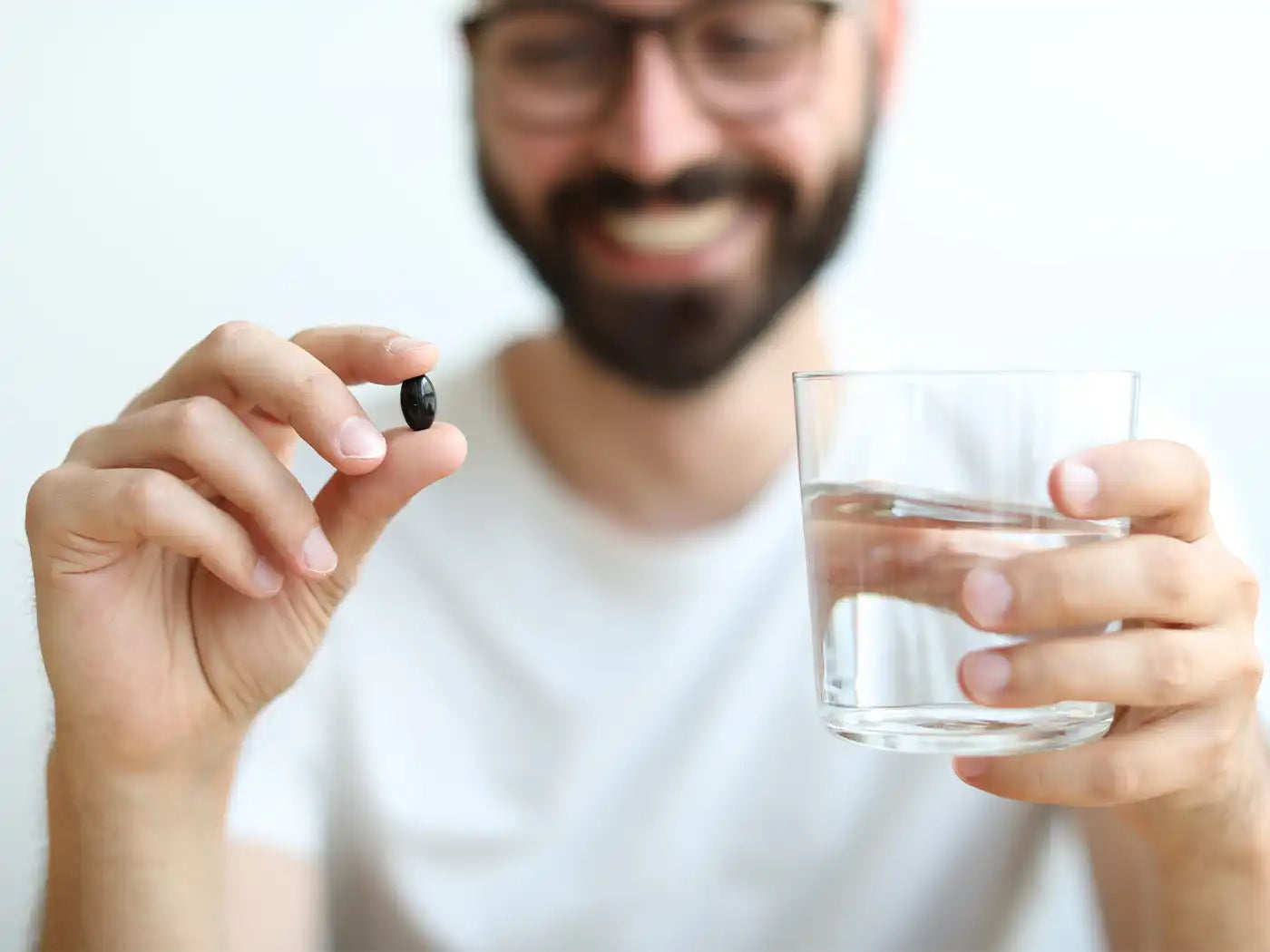 Mand holder softgel og glas i den anden hånd 