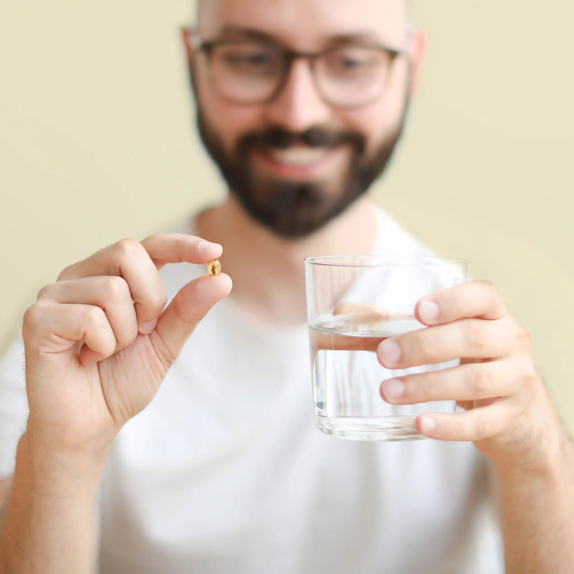 Mand med softgel og et glas vand i hånden