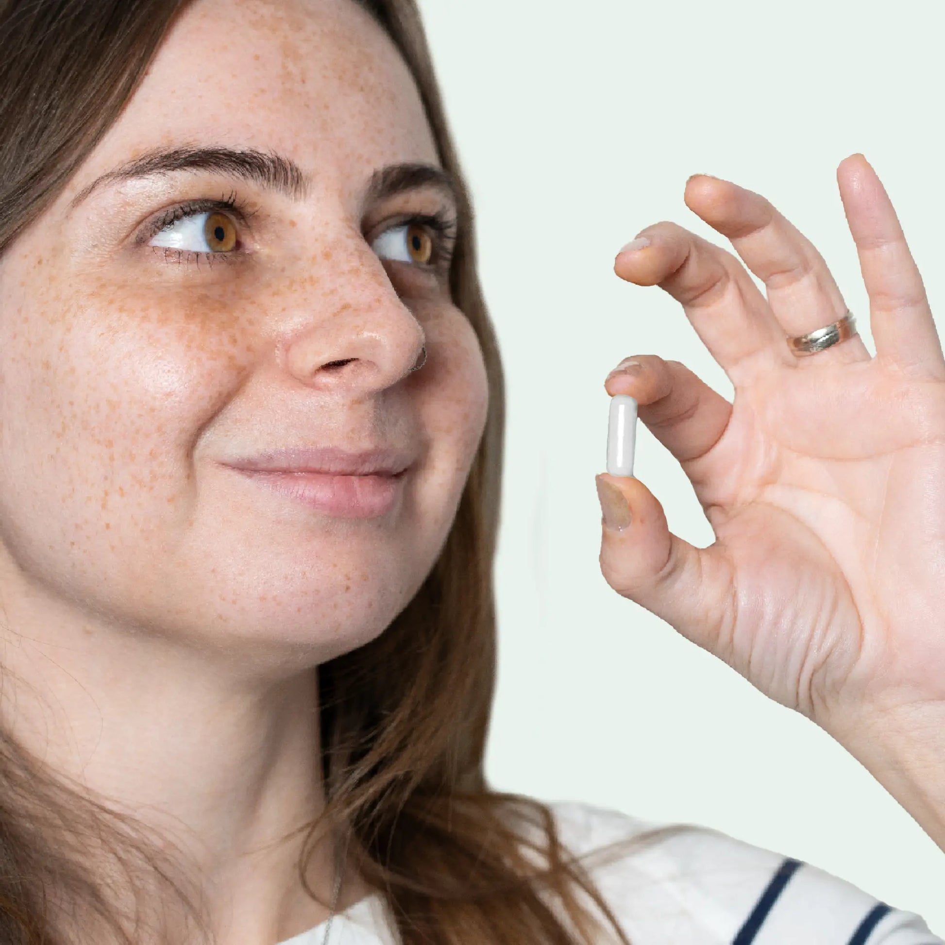 Kvindelig person holder en hvid kapsel mellem fingrene tæt ved ansigtet.