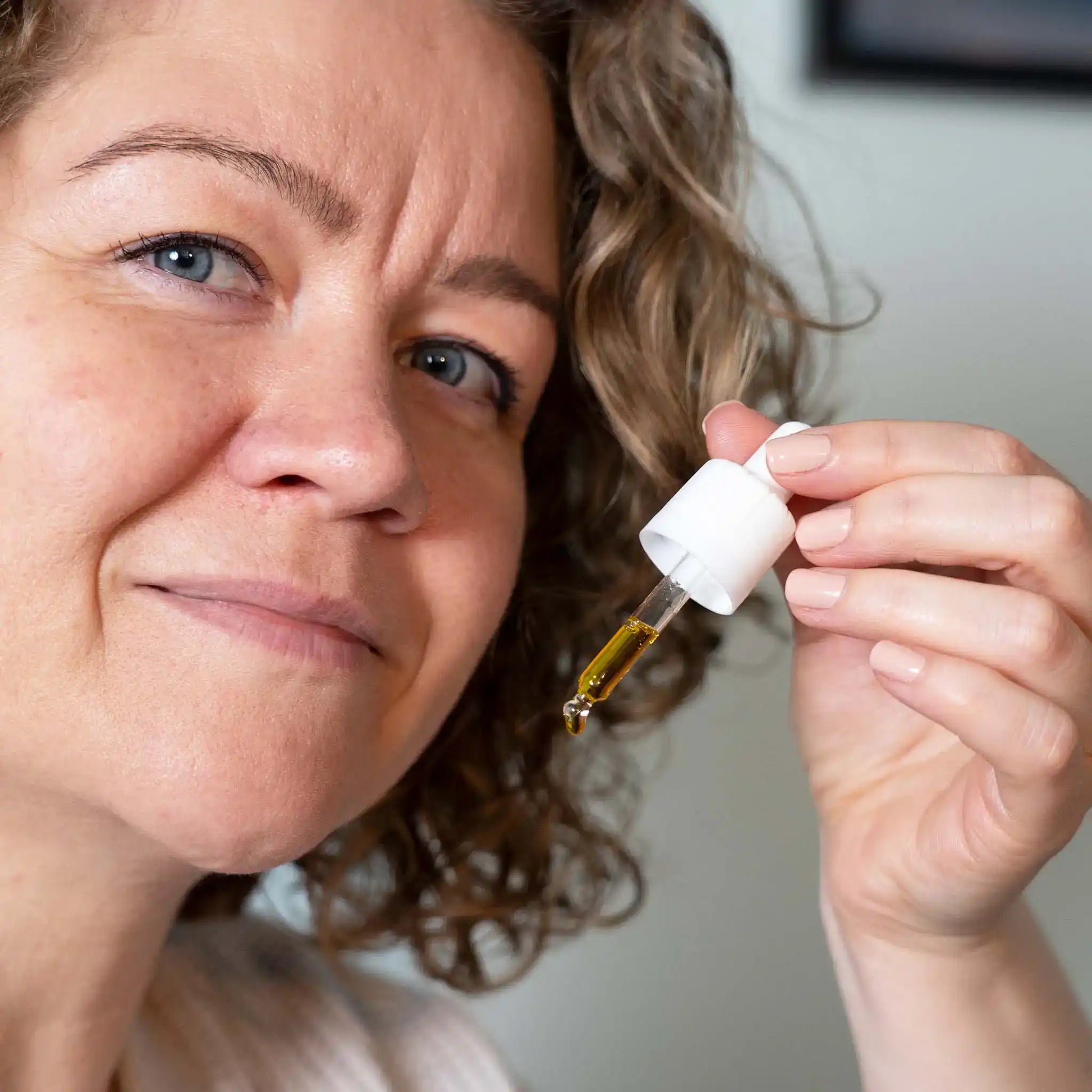 En kvinde holder en flaske CBD Oil 15% Curcumin fra Nordic Oil ved siden af sit ansigt